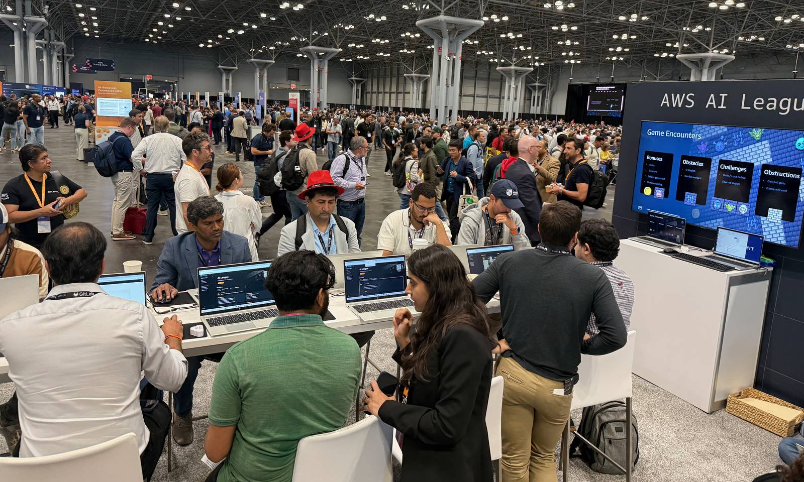 The AWS AI League stand on the packed AWS Summit New York expo floor, with builders at laptops and a Game Encounters screen behind them